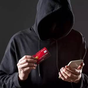 Imagem de uma pessoa encapuzada segurando um cartão de crédito e um celular, representando os possíveis golpes relacionados ao Empréstimo Consignado CLT.