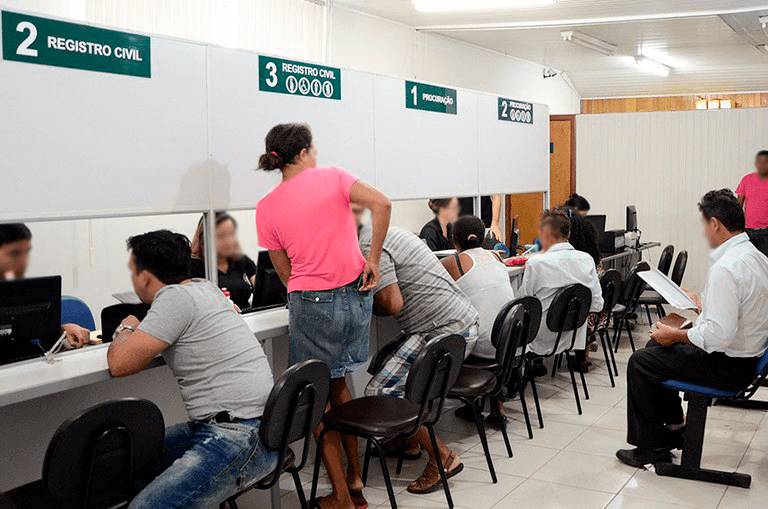 Pessoas em atendimento nos guichês de um cartório, ilustrando a etapa de registro de contratos ou protestos ligados à busca e apreensão.